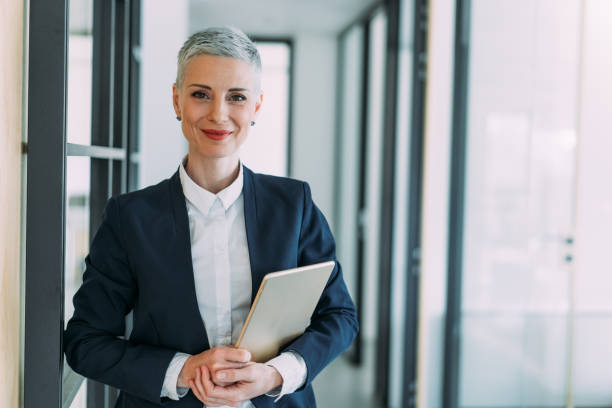 Confident businesswoman in modern office. Shot of beautiful smiling businesswoman holding digital tablet in the office. director stock pictures, royalty-free photos & images