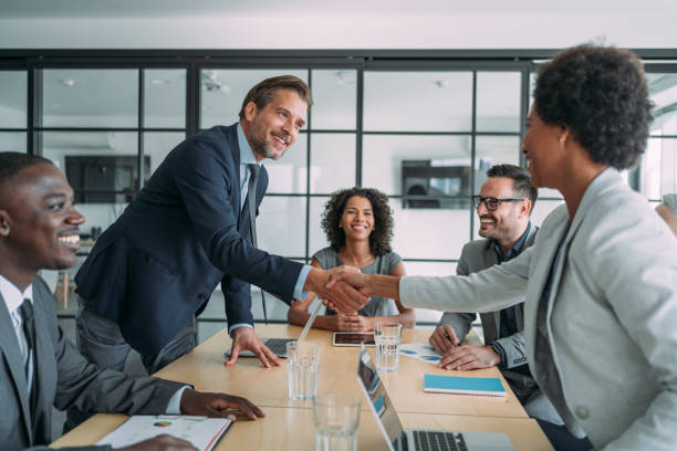 Businesswoman and businessman shaking hands across the table. Entrepreneurs handshaking during a meeting with their colleagues in the office. Business persons shaking hands on a meeting. merging stock pictures, royalty-free photos & images