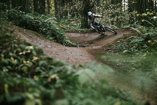 An African American mountain bike rider enjoys an overcast ride through forest trails in Washington state, USA.  He carves through tight dirt berms.