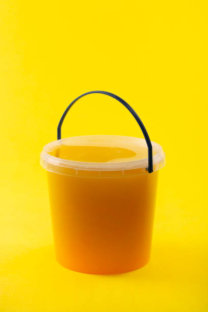 istock Full transparent bucket with bee honey on a yellow background 1444501194