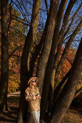 a beautiful young woman in sunglasses stands in an autumn park with a paper cup under coffee. beautiful autumn. High quality photo