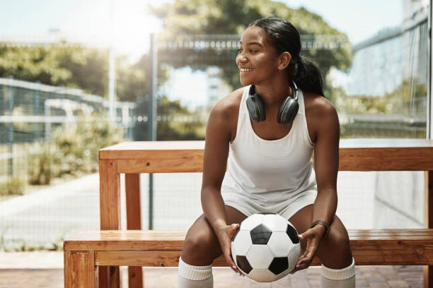 스포츠, 축구, 상파울루의 도시 공원에서 공을 가진 벤치에 있는 여자. 브라질의 피트니스, 재미, 행복한 흑인 여성이 앉아 축구공을 들고 헤드폰으로 여름 햇살을 받으며 경기를 관람하고 있다 - soccer bench soccer player sport 뉴스 사진 이미지