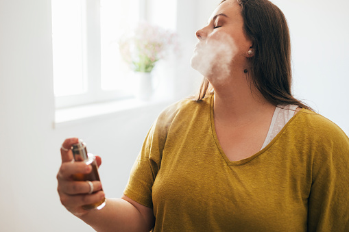 Young Caucasian woman spraying perfume on herself.