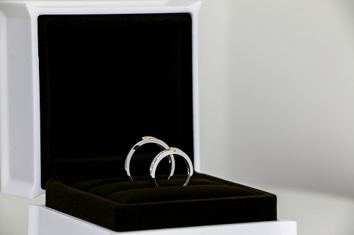 A couple of pristine and exquisite his and hers shiny wedding rings displayed in open ring box on the left. Symbol of romance, love and marriage. Selective focus.