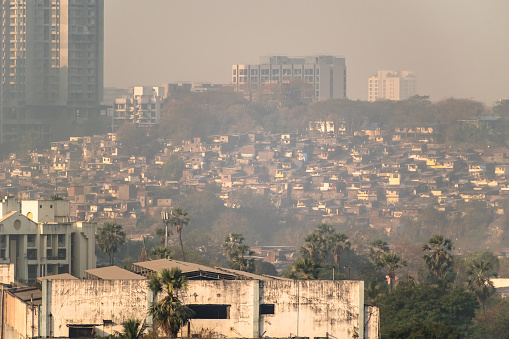 Distant hazy view of slums clustered on a hill surrounded by high rise buildings in the suburb of Kandivali in the city of Mumbai.
