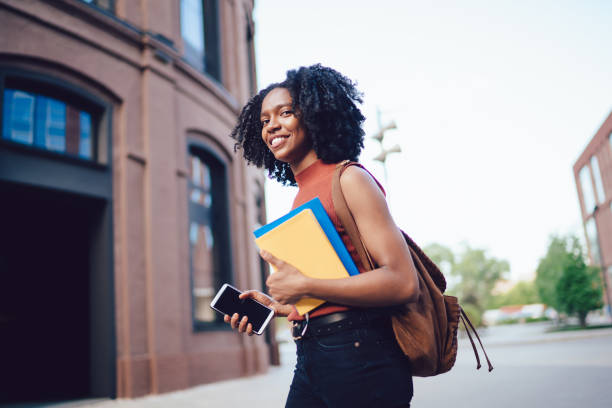 istock Smiling black lady with cellphone and books 1444517281