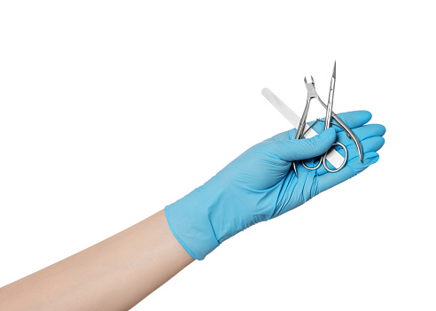 A set of manicure tools in hand with glove: scissors, cuticle removal tool, nailfile.