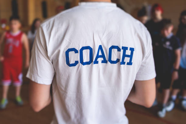 squadra di pallacanestro junior con un allenatore, gruppo di bambini squadra di bambini che si allena e discorso di squadra con istruttore di allenatore, allenatore di basket che spiega le tattiche del piano di gioco sugli appunti dell'allenatore - little boys people indoors soccer foto e immagini stock