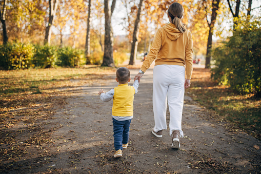 Two people, mother and her little son taking a walk together on autumn day in park.