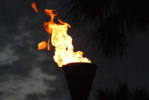 Fire and Flame- Close up of a tall, free standing, black metal torch with a large bright flame against a cloudy night sky.