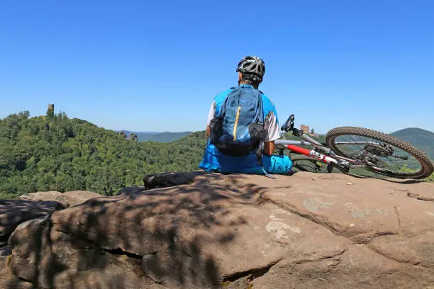 Symbol image: Mountain biker sitting on a rock in the Palatinate Forest with a view of Trifels Castle, Annweiler (Model released)