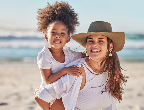 Mom, girl and beach bonding in carrying game by sea or ocean in Mexico for summer family holiday. Portrait, smile or happy woman, mother or parent with afro child, kid or daughter in nature landscape