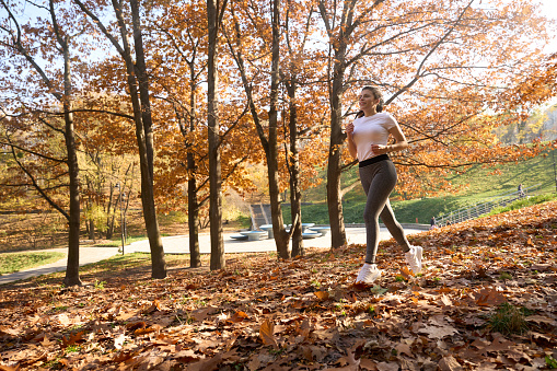 Slender woman in comfortable clothes runs through the fallen autumn leaves, she is wearing light sportswear