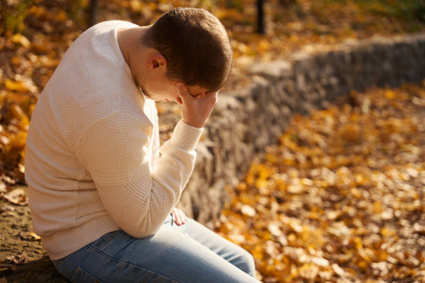 istock Suffering man sits in park on parapet and holds his head 1444525811
