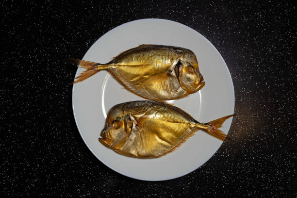 Two smoked fish on a white plate. Vomers (Selene peruviana) are a genus of marine fish that belong to the scad family (Carangidae) stock photo