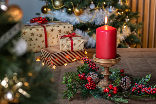 Four red Advent candles are burning. Aside laying pine cone and twig with star anise. On table with red tablecloth. Soft focus on first candle. Useful Christmas background for greeting card.