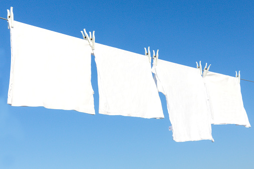 Clean child's clothes hanging on laundry line against light blue background