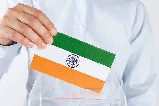 Human hand is inserting Indian flag into ballot box.