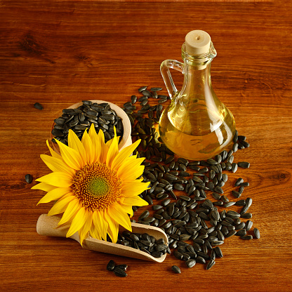 Sunflower seeds, oil in a jug and sunflower flower on a wooden table.