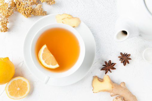 Directly above view of a tea cup with herbal tea and a slice of lemon in it. Surrounded by herbal tea ingredients like chamomile, chamomile tea, lemon, mint leaf, anise, ginger slice and dry orange slices.