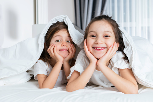 Two cute little girls laughing having fun together in bedroom.