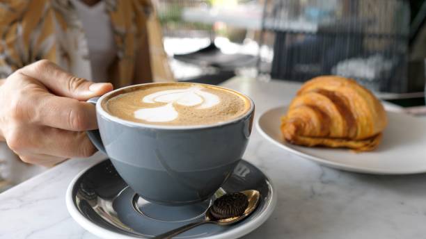 istock Women's hands put on the table a mug of latte with delicate white vegetable-based milk foam. A freshly baked French croissant lies on a white porcelain plate nearby. 1444534228