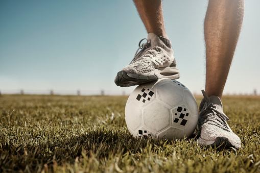 Soccer, ball and shoes in sport motivation on grass for training, exercise and fitness in the outdoors. Legs of football player standing for healthy sports workout, practice or game on a green field