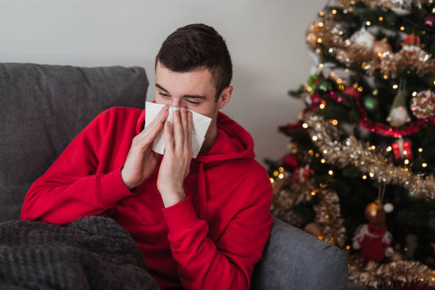Man having a flu and blowing his nose when at home for Christmas stock photo