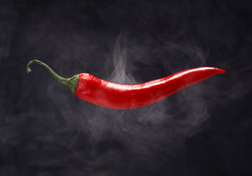 Chilli flakes are poured into a wooden dish. Chilli flakes and dried chili peppers on a brown background. Copy space.