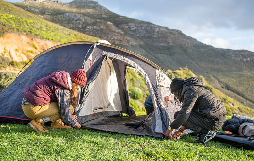 Diverse group of young friends setting up their tent at a campsite in some mountains during a camping trip together