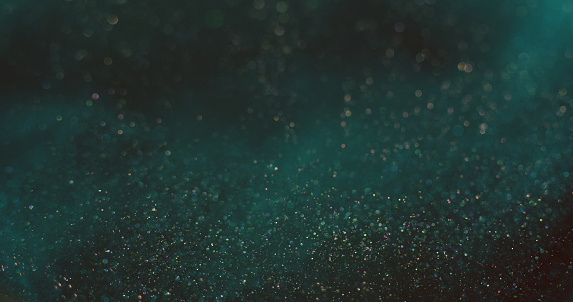 Bokeh light background. Shiny particles texture. Cosmic stardust. Defocused blue orange color shimmering glitter circles on dark abstract wallpaper.