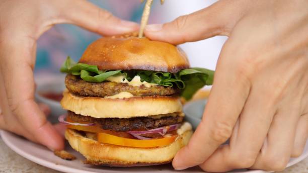 istock Two hands take a two-tiered plant-based burger off the plate. Pressing it on both sides, so that it is convenient to bite it and not to break. Ketchup and french fries are served as a side dish. 1444572947