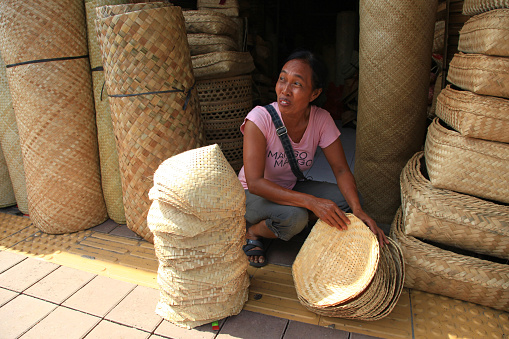 A Balinese woman market vendor selling traditional wicker and rattan hand crafted products in Sukawati village in Bali, Indonesia.
