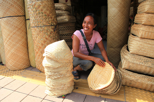 A Balinese woman market vendor selling traditional wicker and rattan hand crafted products in Sukawati village in Bali, Indonesia.