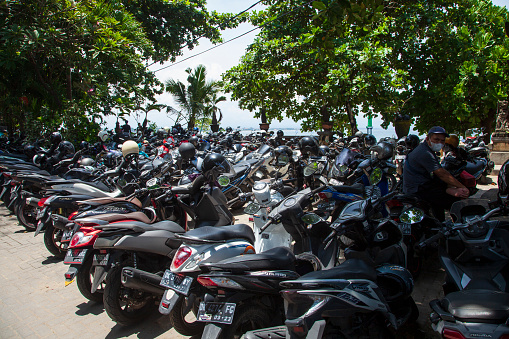 Parked motorbikes and scooters at the end of Jl. Hang Tuah near the beach at Sanur Port in Bali with one man sitting on his motorbike.