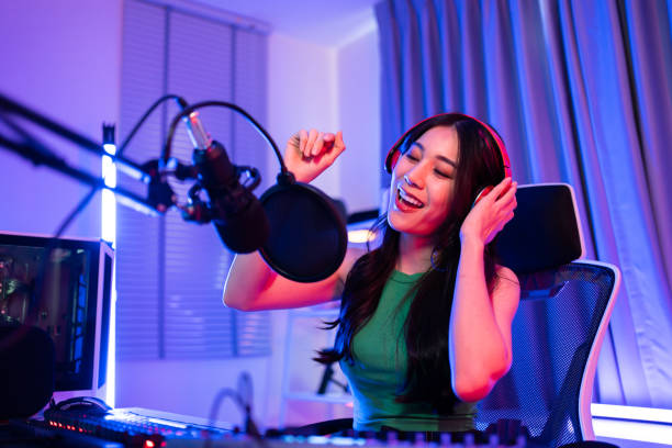 giovane donna asiatica dj audio canta una canzone al microfono per la trasmissione. attraente bella blogger influencer donna che indossa le cuffie e registra podcast di notizie mattutine per la radio nello studio di casa - mid adult audio foto e immagini stock