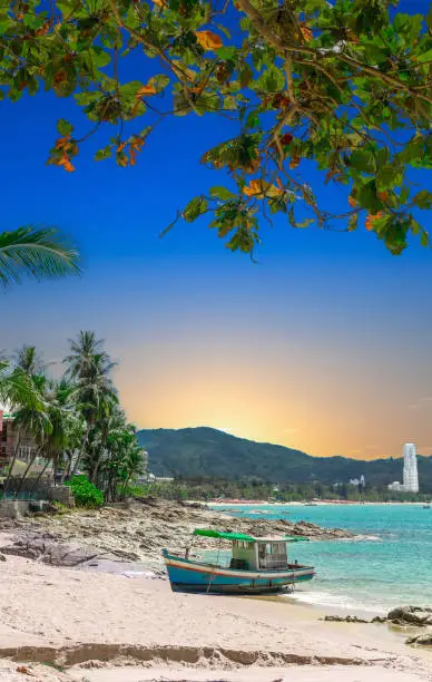 Colourful Sunrise over Patong Beach in Phuket Thailand with boat on the beach sand in the foreground