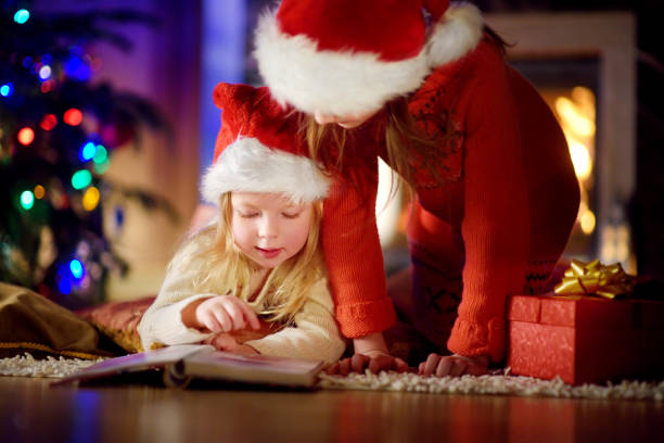 istock Two cute little sisters reading a story book together under a Christmas tree 1444594525