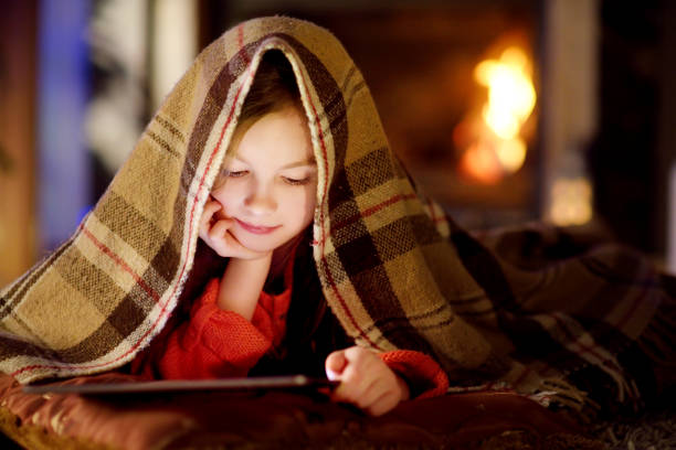 istock Adorable little girl using a tablet pc by a fireplace on Christmas evening 1444594559