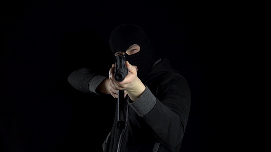 A man in a balaclava mask stands with an AK-47 assault rifle. The bandit stands with a gun on his shoulder, and then aims at the camera. On a black background. 4k