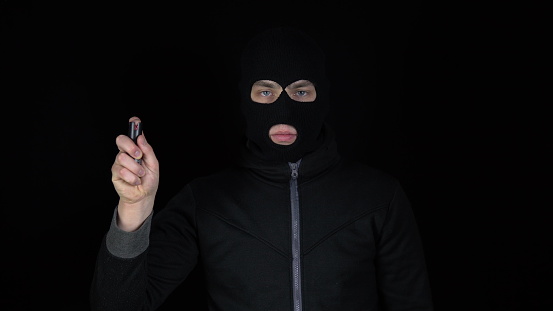A man in a balaclava mask stands with a pepper spray. Pepper spray self defense weapon. On a black background. 4k
