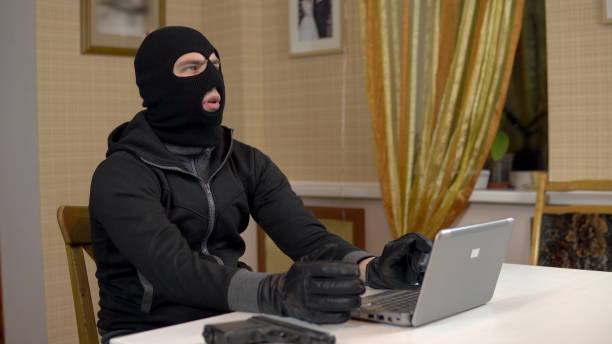 istock A robber is trying to hack into a laptop. A masked thug is sitting in a house and cannot hack into a laptop. Theft of data from a computer. 1444598538