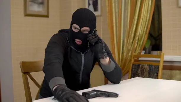 Burglar talking on the phone. A masked thug sits in a house and threatens the telephone with a gun. Extortion by phone. 4k