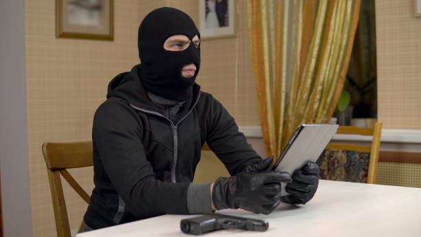 istock A robber is trying to hack into a tablet. A masked thug is sitting in a house and cannot hack into a tablet. Theft of data from a tablet. 1444599224