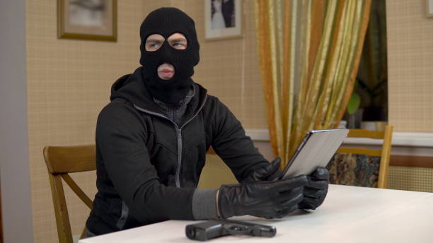 istock A robber is trying to hack into a tablet. A masked thug is sitting in a house and cannot hack into a tablet. Theft of data from a tablet. 1444599228