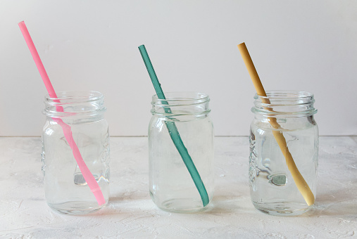 Three mason jars with drinking straws made of plastic, glass, and bamboo.