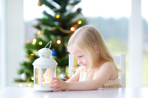 Beautiful little girl lighting a candle in white lantern on Christmas day