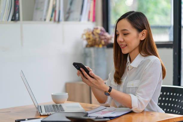 istock Asian female holding her smartphone while using her laptop. 1444613443