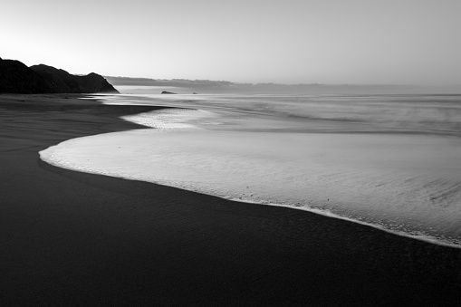 Waves gently sweep across the cold dark sands at sunrise in Point Reyes.