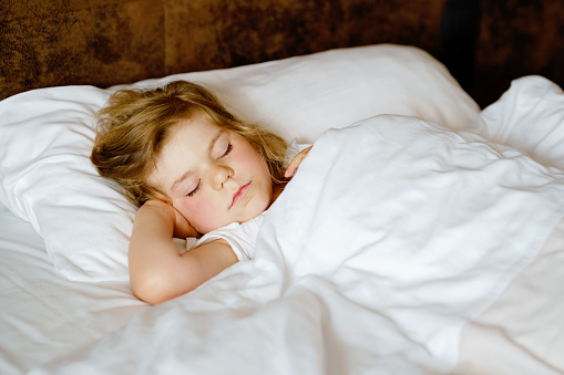 Cute little toddler girl sleeping in bed. Adorable baby child dreaming, healthy sleep of children by day. Deep sleeping of toddler. Kids resting